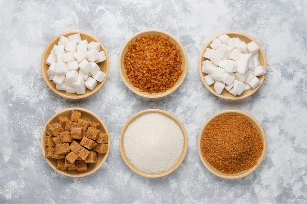 potes de açúcar - cristal, mascavo, refinado e de confeiteiro - em uma mesa branca