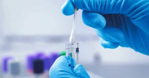 A imagem mostra as mãos de um profissional da saúde reservando em um tubo de ensaio a coleta de um exame de DNA.