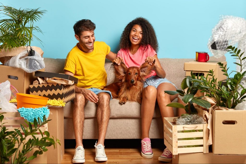 Casal feliz sentado no sofá em meio à caixas de mudança com seu animal de estimação, cachorro