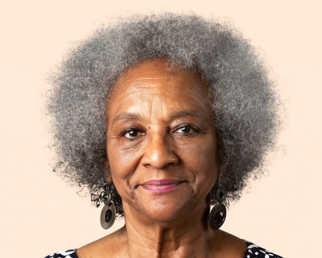 Mulher idosa negra, com cabelos grisalhos crespos e pele madura, sorrindo. 