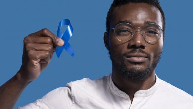 A imagem mostra um homem negro segurando uma fita azul com uma das mãos.