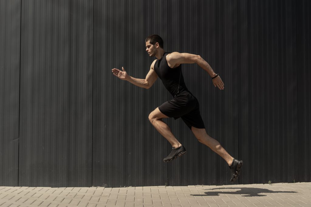 A imagem possui um homem atleta, de pele branca, utilizando roupas pretas, enquanto se exercita com a corrida ao ar livre.