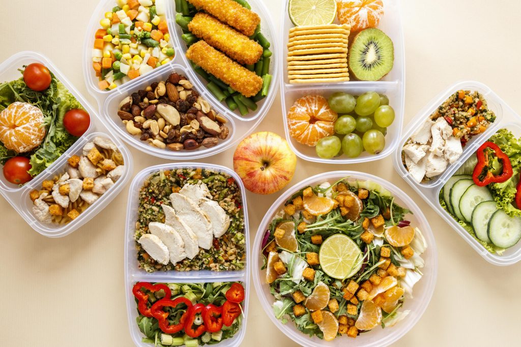 Fotografia com uma vista de cima em que é possível ver inúmeros alimentos, desde carnes a frutas e verduras dentro de potes. Um ambiente muito colorido.