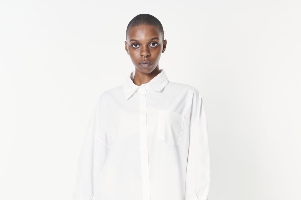 Mulher negra usando uma camisa branca de botão, atrás de um fundo branco