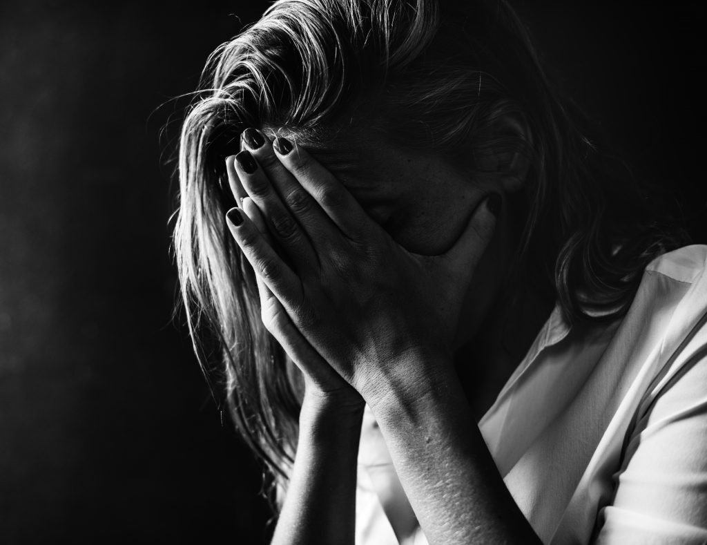 Foto em preto e branco de mulher com as mãos no rosto em sinal de tristeza