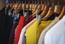 A imagem apresenta roupas em cabides pendurados em um armário, sendo elas nas cores preta, vermelha, rosa, amarela, branca e jeans.
