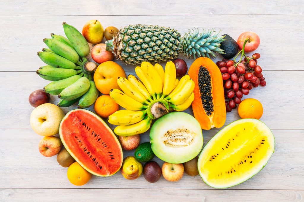 Frutas juntas em cima de uma mesa: abacaxi, banana, mamão, maçã, pera, uvas, laranja, melão e abacate