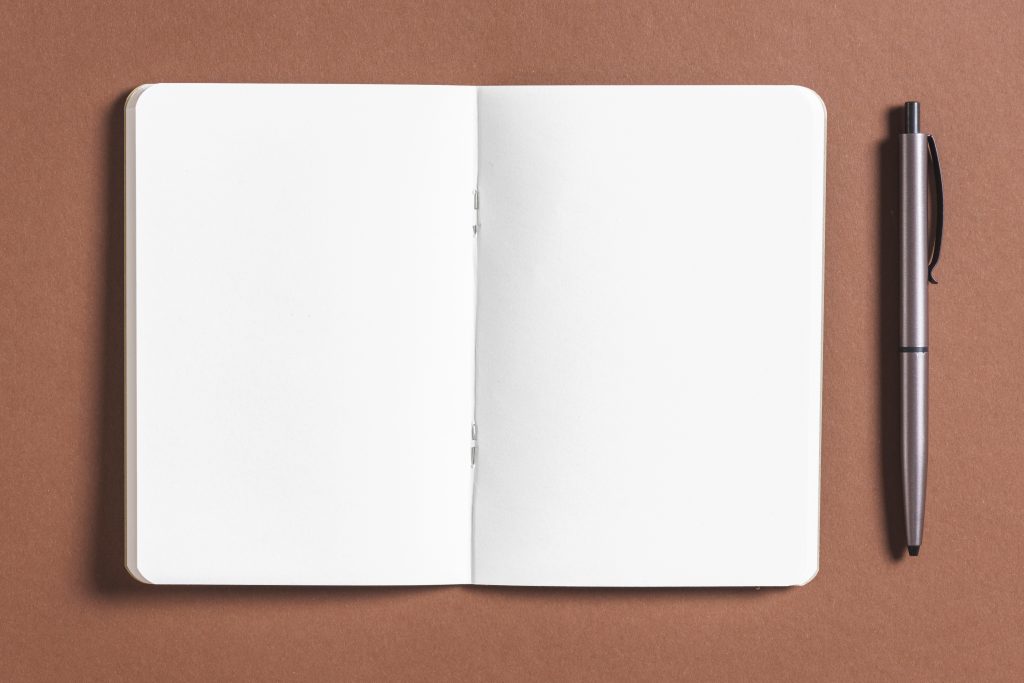 caderno sem linhas, em branco, aberto com uma caneta ao seu lado.